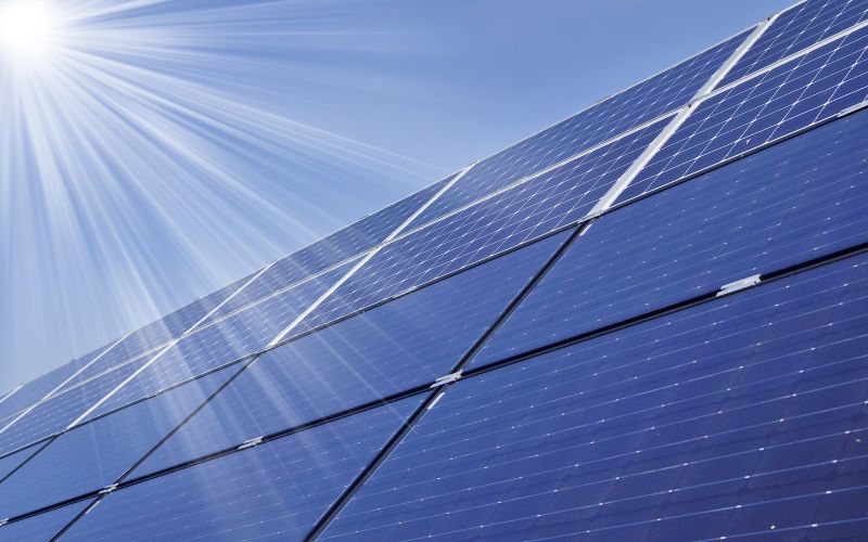 Solar panels installed at an angle under a clear blue sky with sun rays shining down.