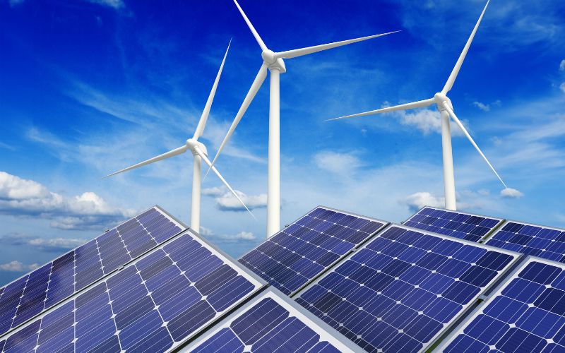 Solar panels and wind turbines against a backdrop of a cloudy blue sky, symbolizing renewable energy sources.