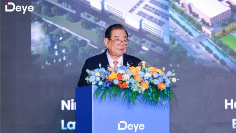A professional speaker at a corporate event, standing behind a podium decorated with vibrant flowers, delivering a keynote speech on innovation and sustainable building solutions for Deepblue.
