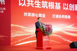 A man in a suit presents at a podium decorated with flowers during a conference on innovative construction and sustainable building practices. The event emphasizes collaboration and core technology in the construction industry.